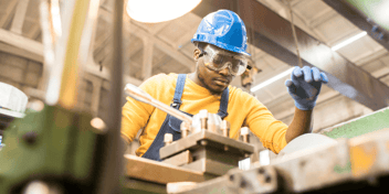 Worker with a blue hard hat and yellow shirt working in a manufacturing plant.