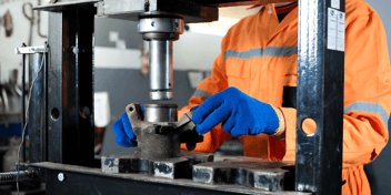 A worker in an orange flame retardant suit using a hydraulic press.
